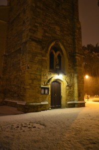 The tower door entrance to the church, with night snow falling